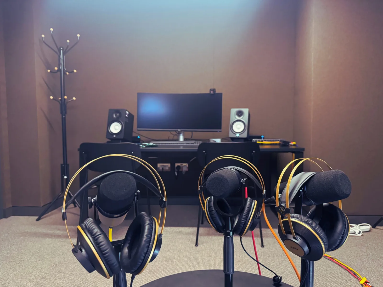 Three podcast microphones with headphones in front of a recording desk with a monitor and studio speakers at Great Portland Street Studio
