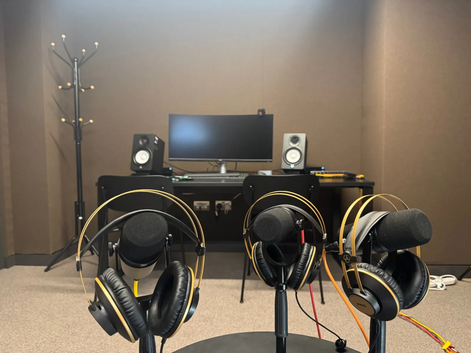 Three podcast microphones with headphones in front of a recording desk with a monitor and studio speakers at Hale House